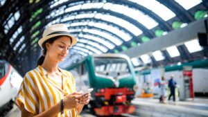 una donna con un cappello che guarda un telefono alla stazione dei treni