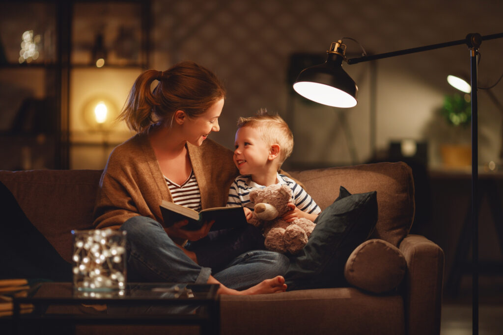 La famiglia prima di andare a letto la madre legge al figlio un libro vicino a una lampada la sera