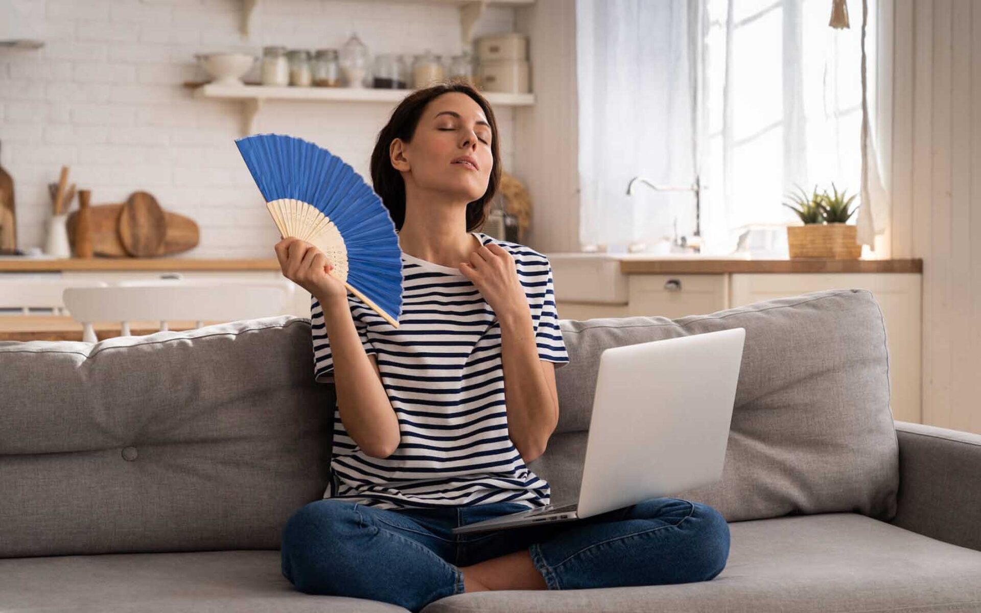 una donna seduta su un divano con un ventilatore e un computer portatile